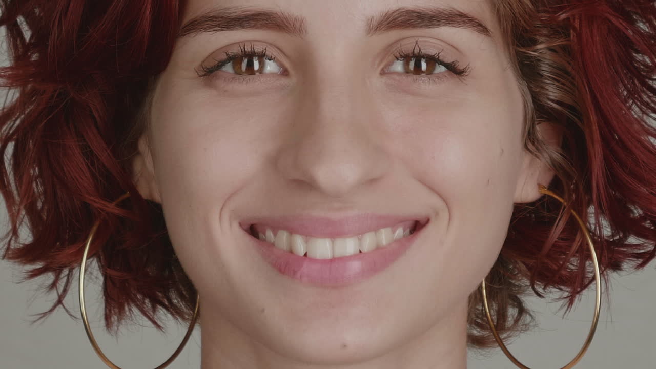 High-quality 4K footage of a joyful young multi-ethnic woman with vibrant, styled hair and bold fashion accessories. She smiles widely, showcasing clean teeth
