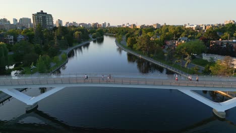 Vista-Aérea-De-Peatones-Caminando-A-Través-De-La-Pasarela-De-La-Flora-Sobre-El-Tranquilo-Y-Reflexivo-Canal-Rideau-En-Ottawa