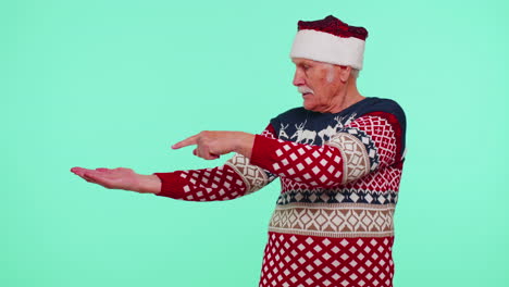 Grandfather-in-Santa-Christmas-sweater-showing-thumbs-up-and-pointing-empty-place,-advertising-area