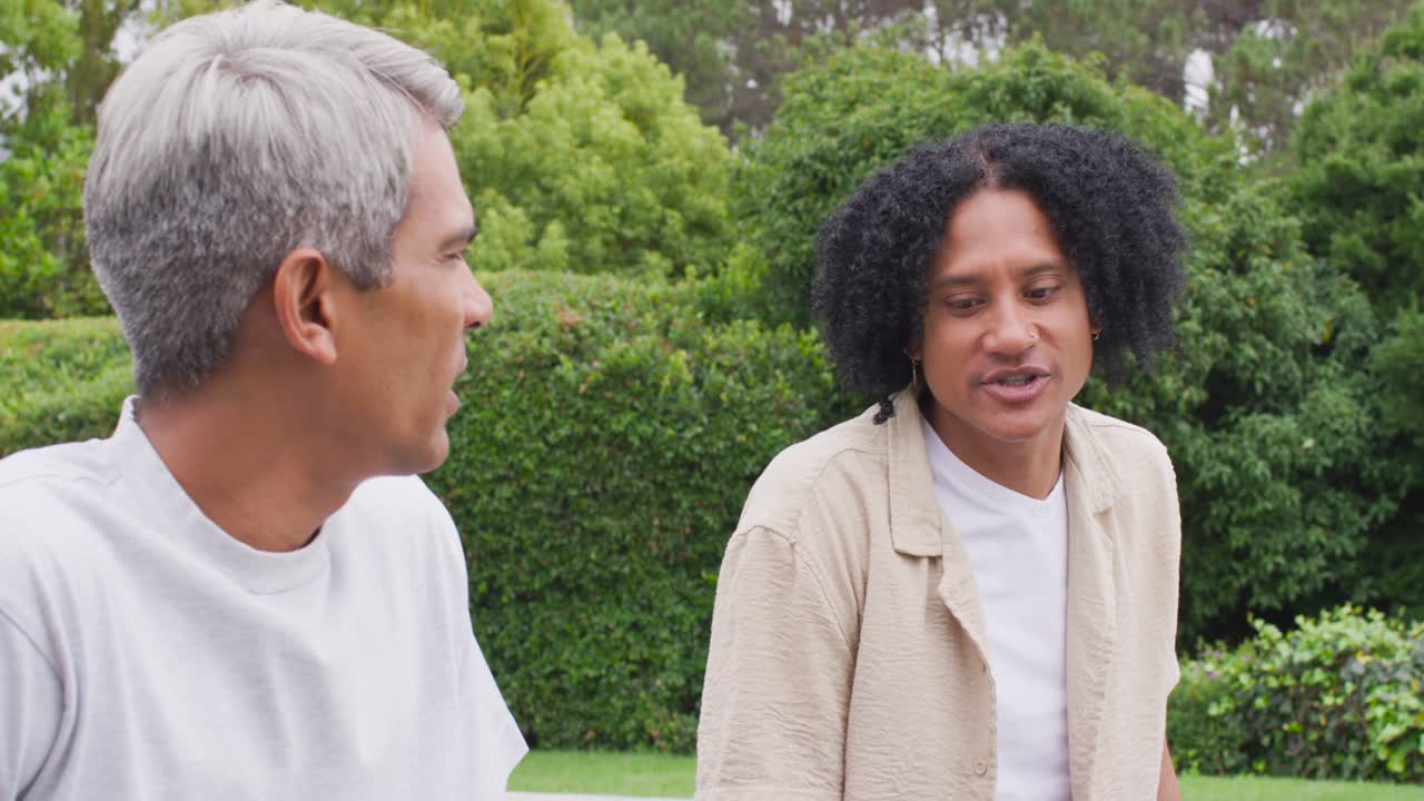 African American male friends sitting pool edge, curly man sharing memory, grey man replying