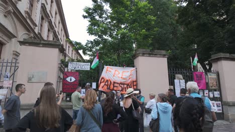 free palestine protest with crowds holding banners and marching, shot from the street as crowds gather around gates