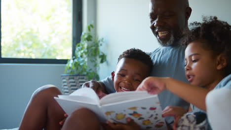 Großvater-Liest-Den-Enkelkindern-Ein-Buch-Vor,-Die-Zusammen-Auf-Dem-Sofa-Sitzen