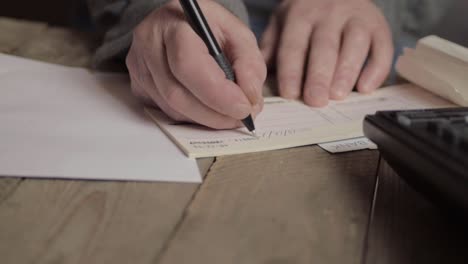 hand of busy person writing a banking check to pay bills in office with phone