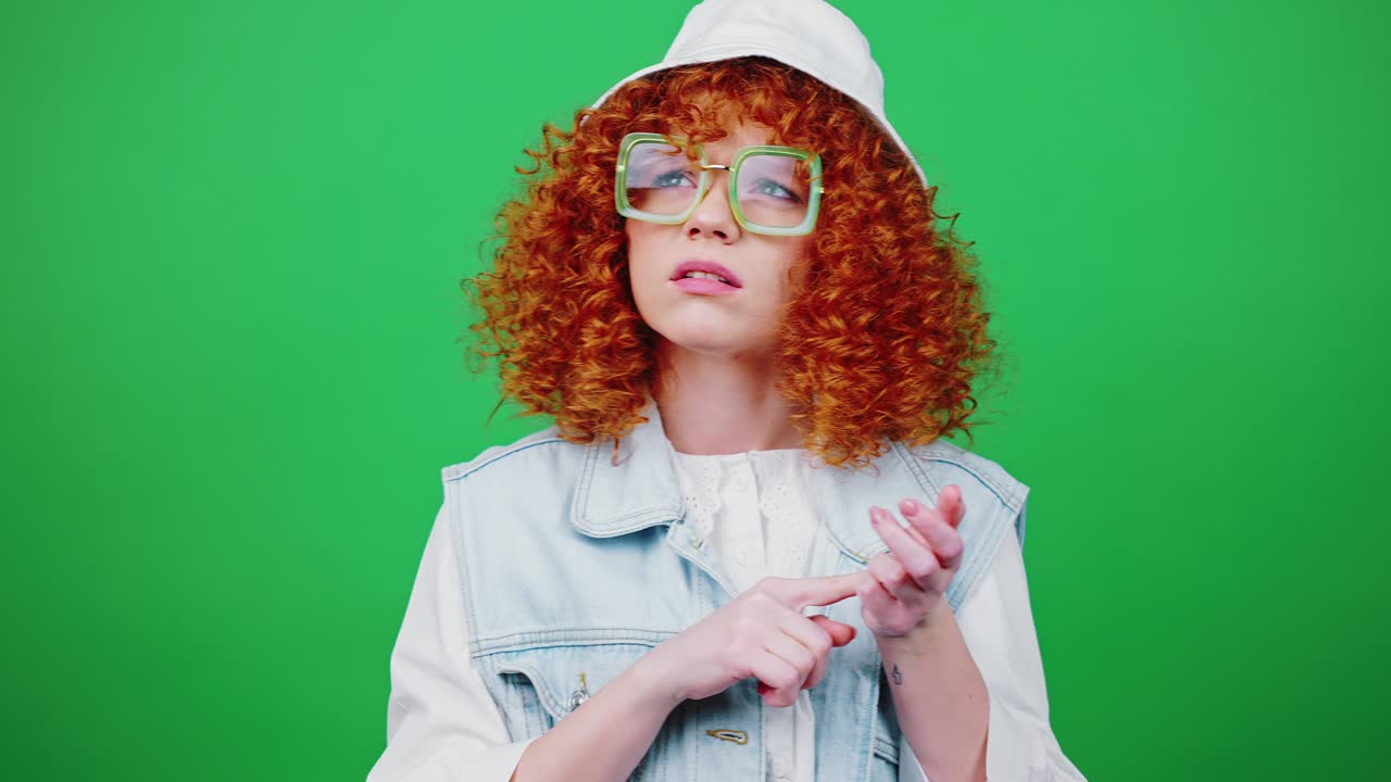 안경과 파나마 모자를 입은 젊은 은 머리 곱슬머리 여성은 손가락에 변형을 세고 머리를 흔들고 있습니다.