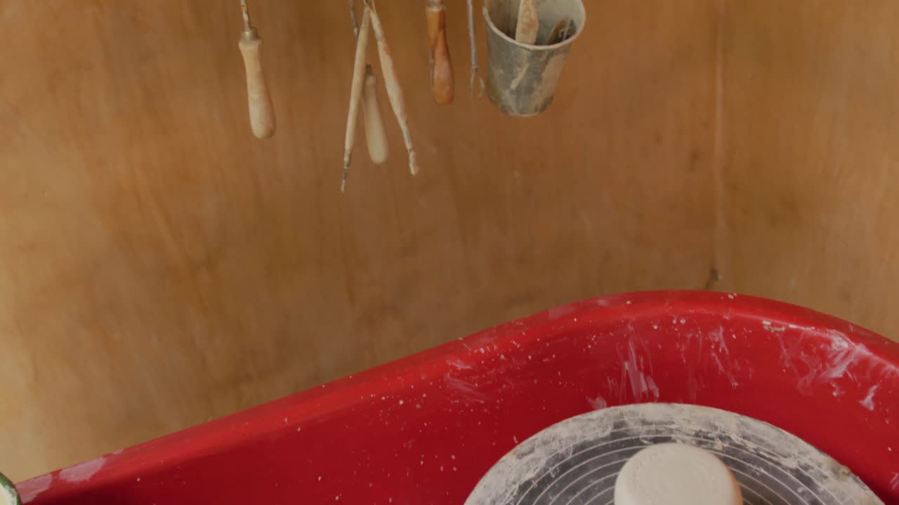 Pottery equipment and hanging tools with handmade pots and plates lying on shelf in pottery workshop