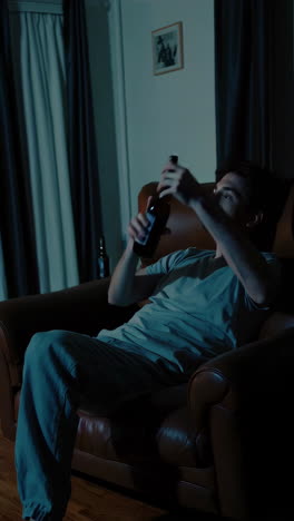 man drinking beer and watching tv at home at night
