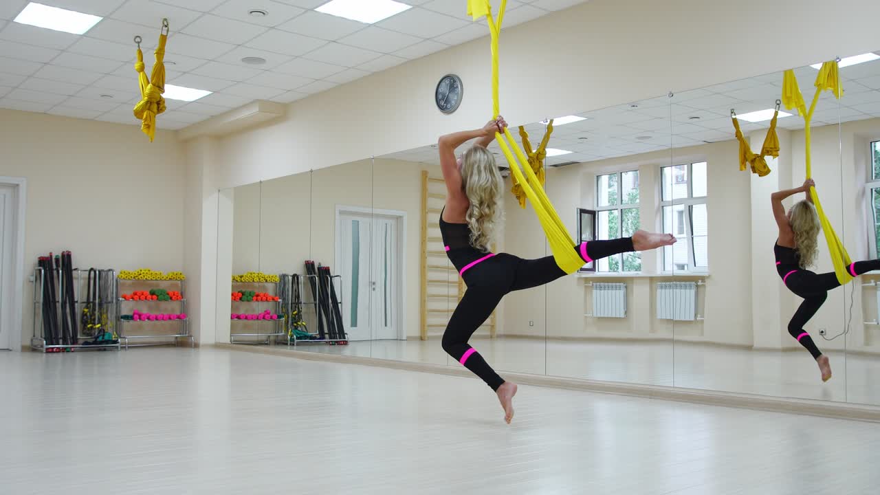 Concetto di sport e stile di vita sano. Spazio per il testo. Giovane donna in forma e graziosa che indossa abbigliamento sportivo mentre fa esercizi di stretching di fly yoga in una palestra/sala fitness bianca in stile loft