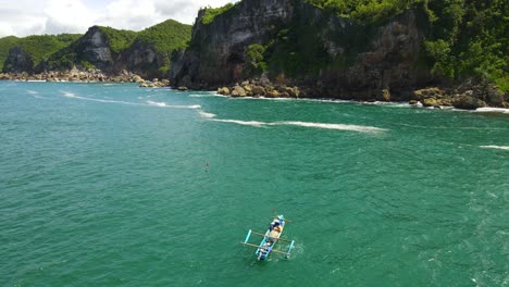 indonesian fishermen in small fishing boat on turquoise ocean by kesirat cliffs