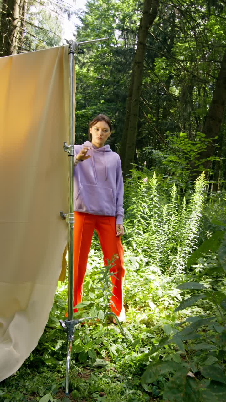 Fashionable woman in forest wearing a purple hoodie and orange pants