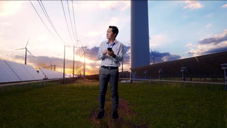 full body of asian male professional worker with his smartphone with solar panel and wind turbines, he observes by looking around before he come to concentrating with his smartphone