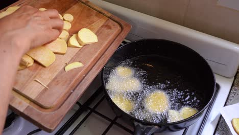 hand putting sliced sweet potato chips into a frying pan with hot cooking oil