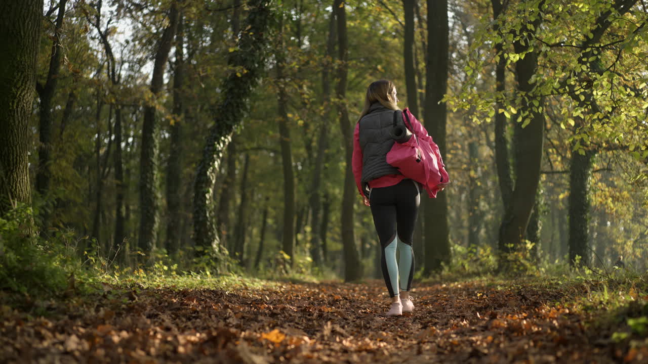 Woman walking through a sun-dappled autumn forest path