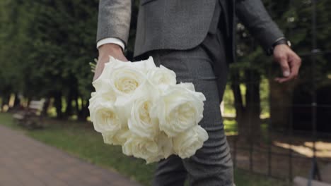 Groom,-young-man-businessman-in-green-summer-park-with-a-wedding-bouquet-in-hands,-wedding-day