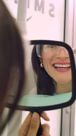 happy young woman checking smile in mirror after treatment, confidence and dental care