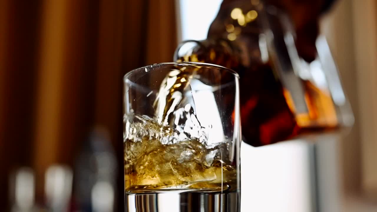 Pouring whiskey in glass with ice cubes, low angle view
