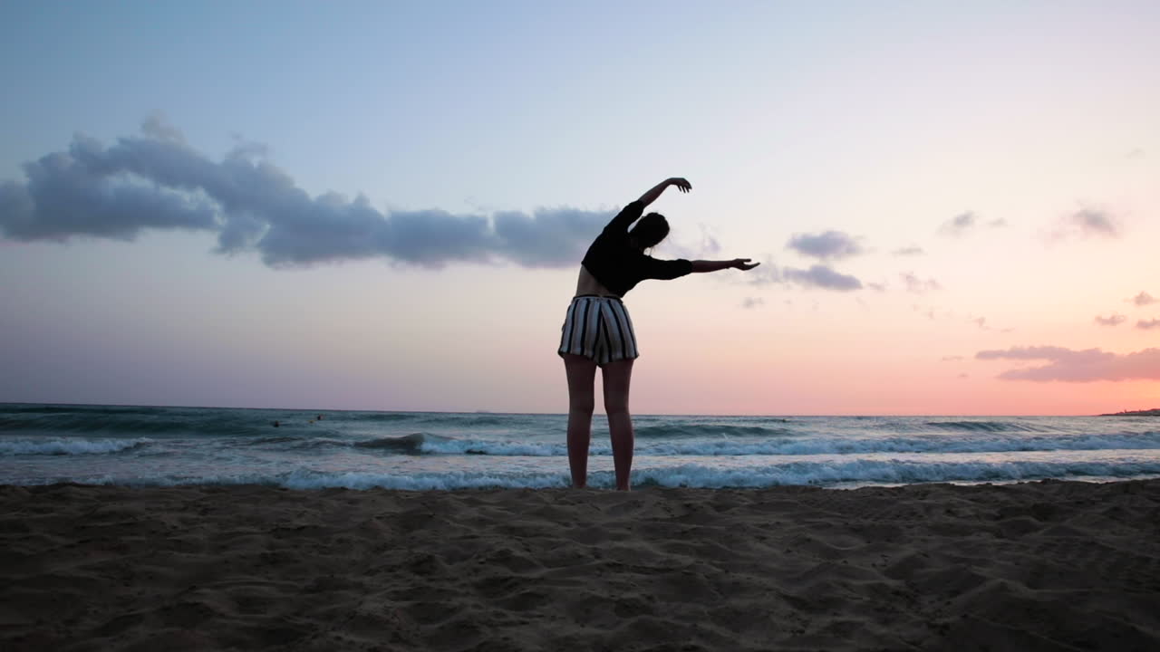 Silhouette of a woman with wide hips and thin waist doing yoga-stretching on the beach at sunset.