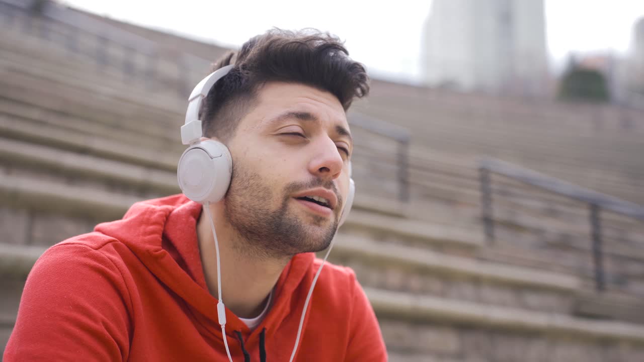 hombre guapo escuchando música con auriculares en un banco al aire libre.