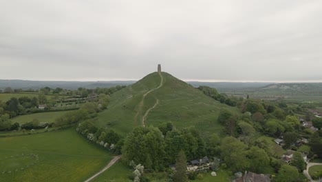 aerial view of glastonbury, drone moving forward towards the st michaels tower, drone flying over the green fields and some houses . 4k, 60fps.