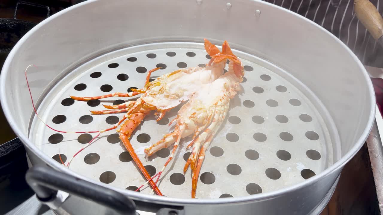 A spiny lobster cooks inside a metal steamer basket with rising steam at street market