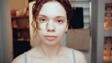 girl applying under-eye patches and looking at camera in bathroom