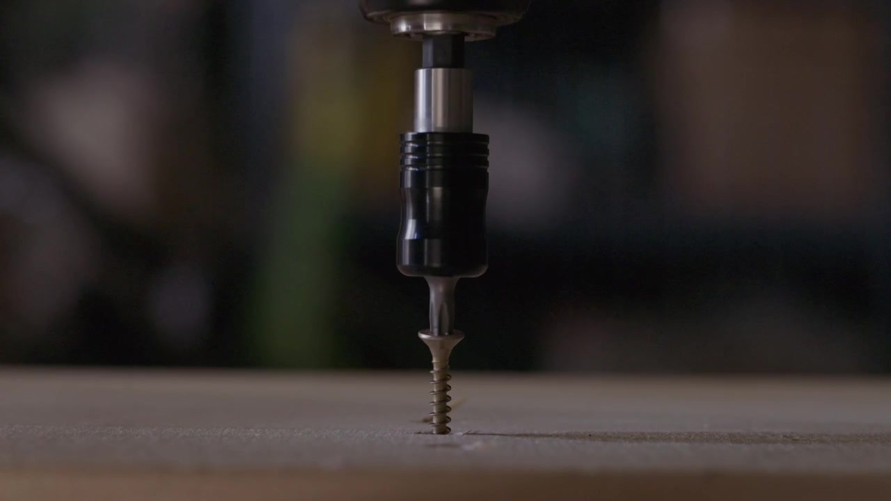 Primo piano di un avvitatore elettrico che inserisce una vite per legno in metallo in una tavola di legno durante lavori di costruzione o assemblaggio di mobili