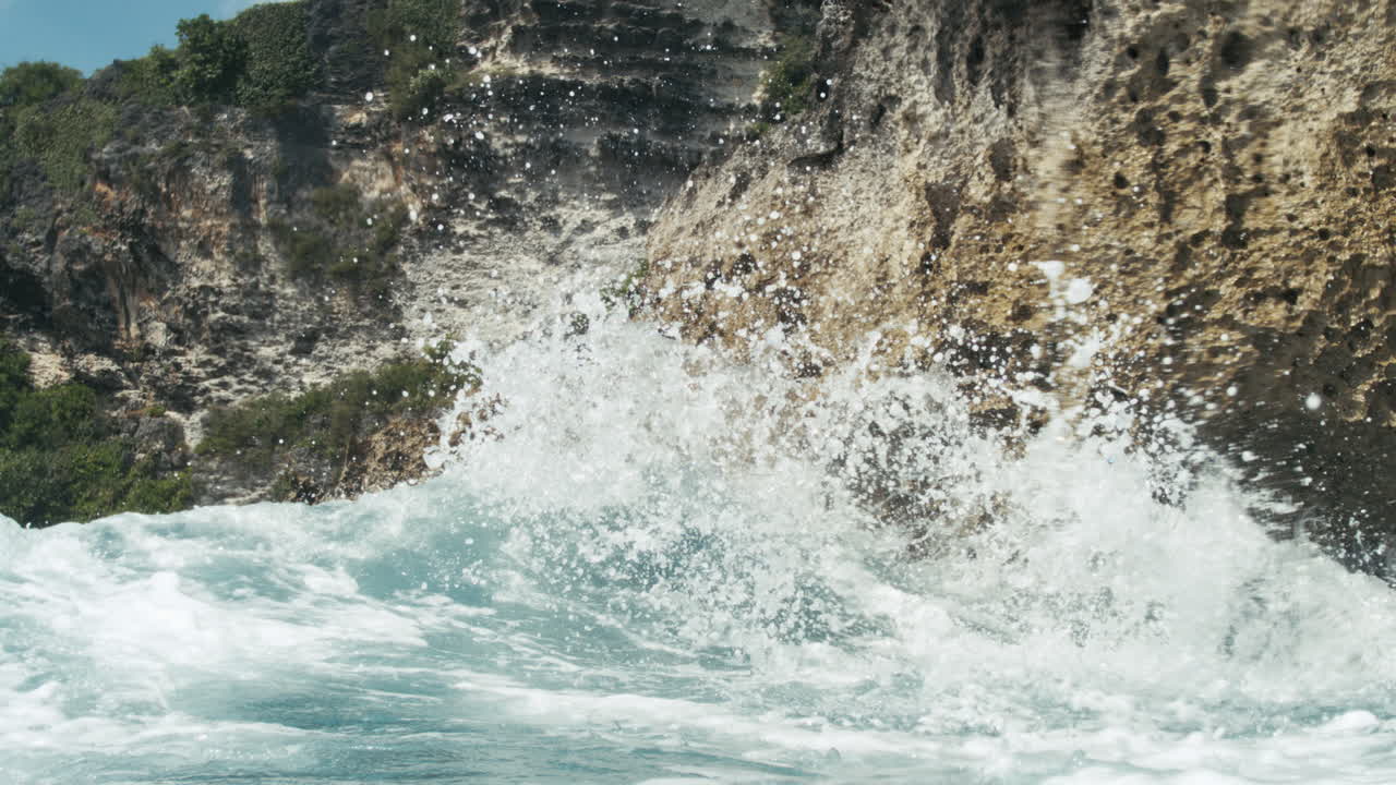 Waves roll into rocky shore beneath steep tropical bluff, slow motion slowmo backdrop