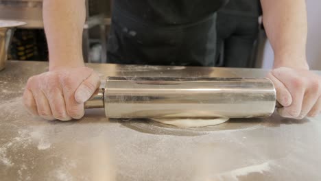 italian pizza chef forming the dough on a floured surface and rolling out a dough