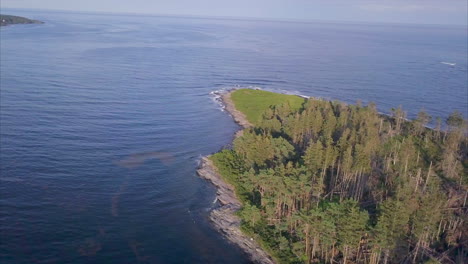 aerial shot orbiting around the blue atlantic ocean waves crashing against the rich green forest of richmond island off the maine coast