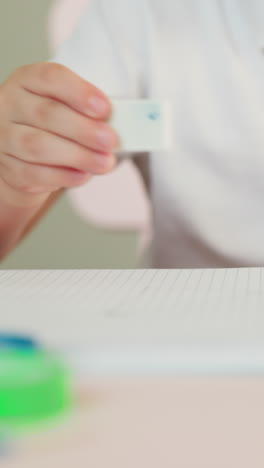 niño pequeño mira y limpia la imagen con borrador en la página del cuaderno en la mesa de primer plano. niño pequeño serio quita el dibujo y la suciedad del cuadro en el preescolar