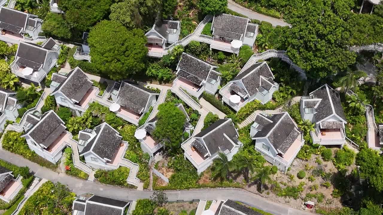 Aerial footage showcases clustered villas surrounded by lush trees and winding pathways.