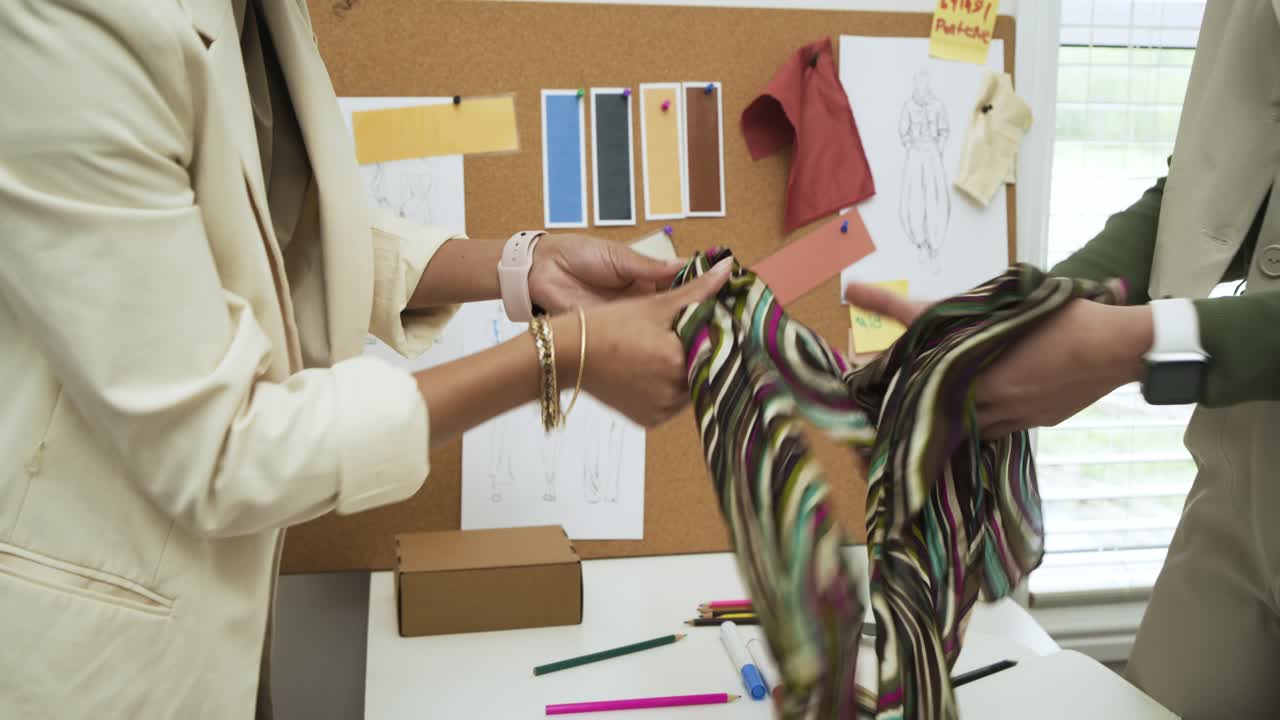 Comparing striped sample with sketches, Diverse female designers pinning it on cork board in studio