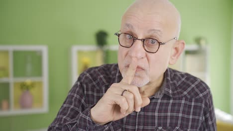 Elderly-man-looking-at-camera-making-be-quiet-at-home-sign-and-warning.