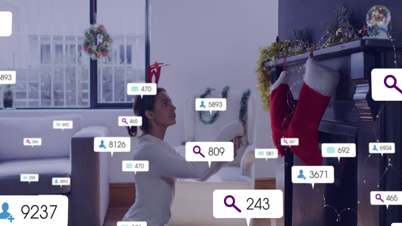 Animation of social media icons with numbers over caucaisian woman decorating house for christmas