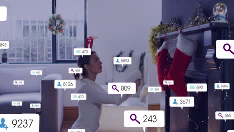 animation of social media icons with numbers over caucaisian woman decorating house for christmas
