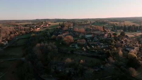 aerial view with elevation of a small village and its church in the middle of the forest at sunrise, saint-avit-ségnieur, dordogne