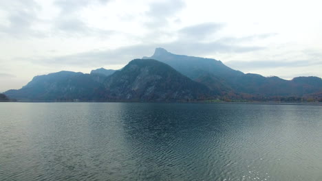 Disparo-De-Drones-Cerca-De-La-Superficie-De-Un-Lago-Junto-A-Las-Montañas-En-Austria,-4k-Uhd