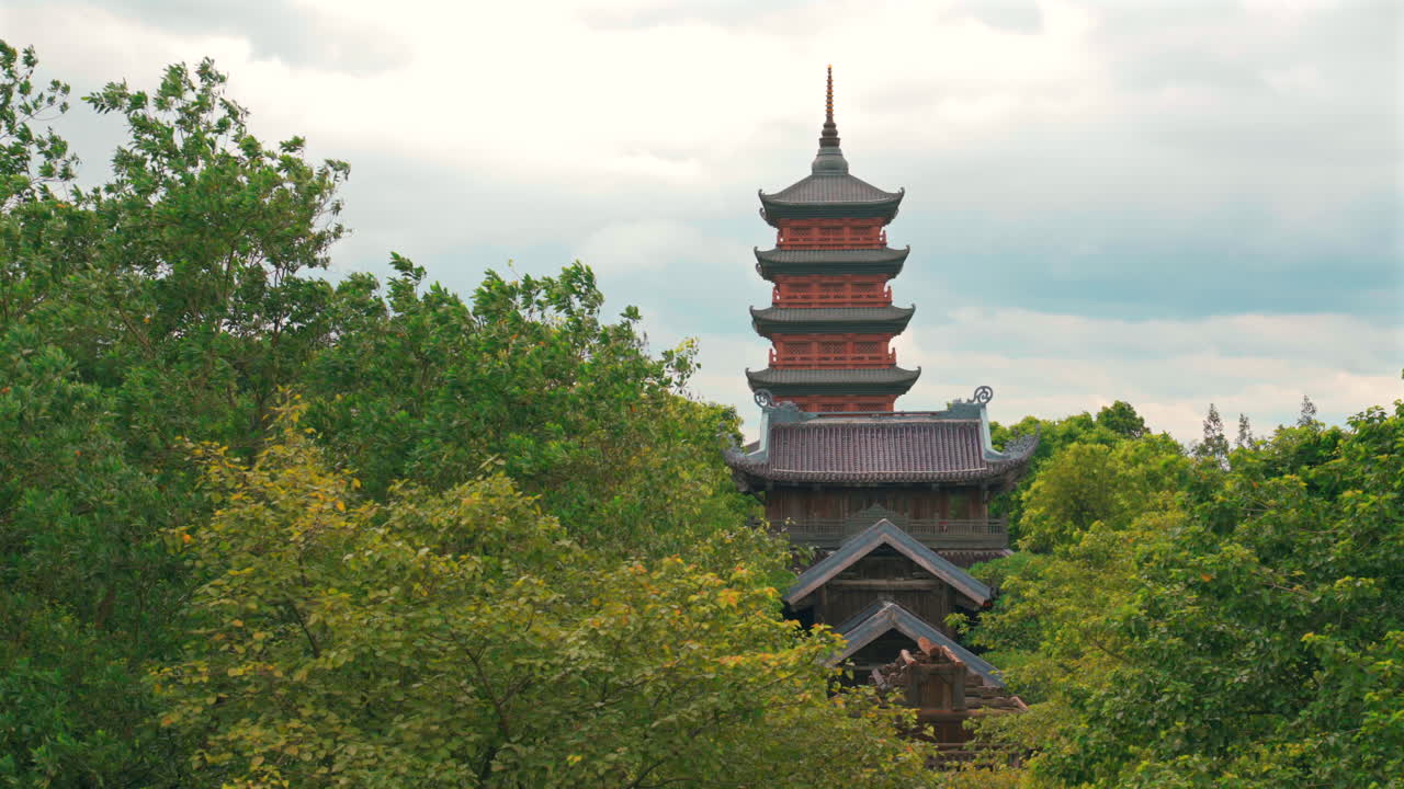 Una toma detallada de la alta y tradicional estupa de varios niveles en la Pagoda Bai Dinh, elevándose sobre los tejados del templo y los frondosos árboles verdes en Ninh Binh, Vietnam.