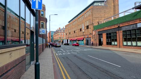 camera moves steadily down a quiet urban street beside a large brick building in leeds, england, under natural daylight with clear visibility