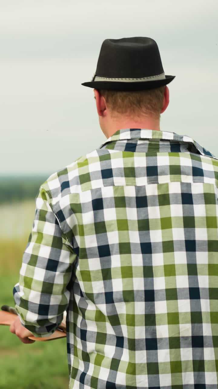 Close-up back shot of a couple walking on a grassy field. The woman, dressed in a white gown, carries a canvas while the man, in a checkered shirt and jeans, hands her a drawing pad as they
