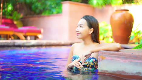 portrait of smiling young thai woman in 30th leaning on swimming pool border while inside water