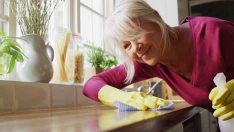 Feliz-Mujer-Caucásica-Mayor-Usando-Guantes-De-Goma,-Limpiando-Encimera-En-La-Cocina