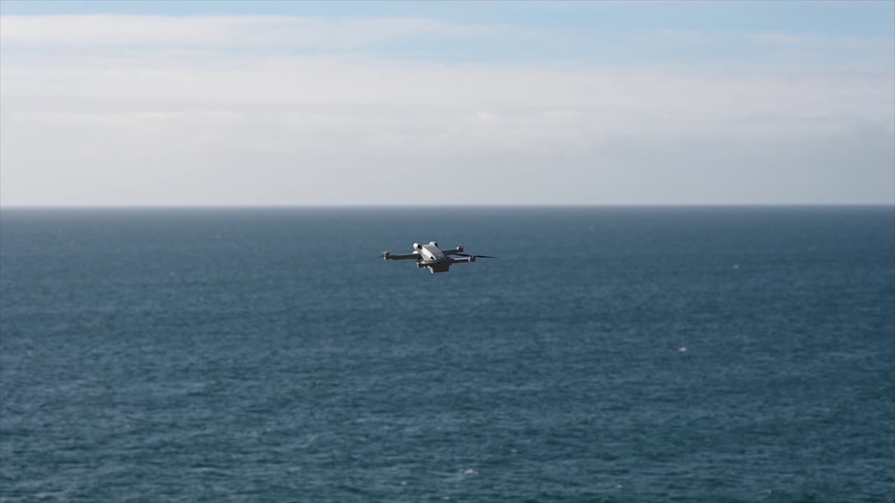 회색 드론이 바다 위를 날고 있고, 프로펠러가 빠르게 회전하고, 영화 제작 장비