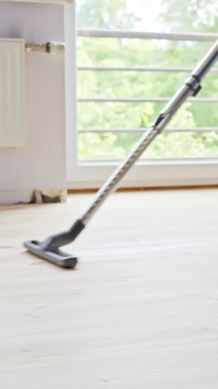 Person vacuuming wooden floor in bright living room, DIY project focus