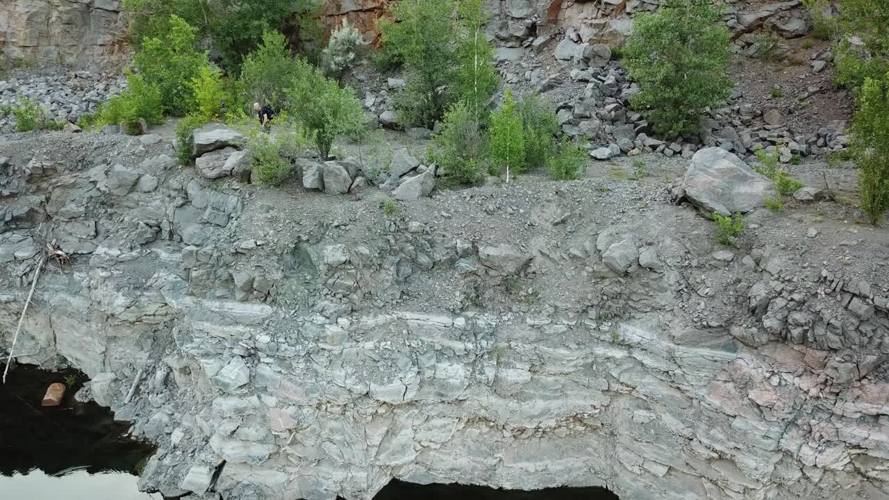 Aerial view of a tourist walks along the rocky shore of a lake. Traveler on the cliff. Camping season