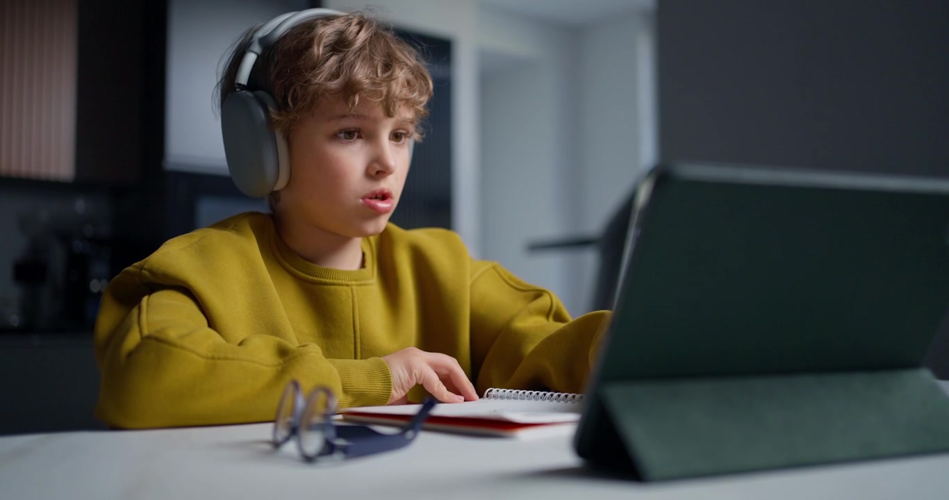 Young Boy with Headphones Studying with Tablet and Notebook