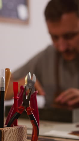 leathersmith takes cutter for leather edge processing from rack in workshop closeup. manual craft instruments of master. kit in manufacturing studio