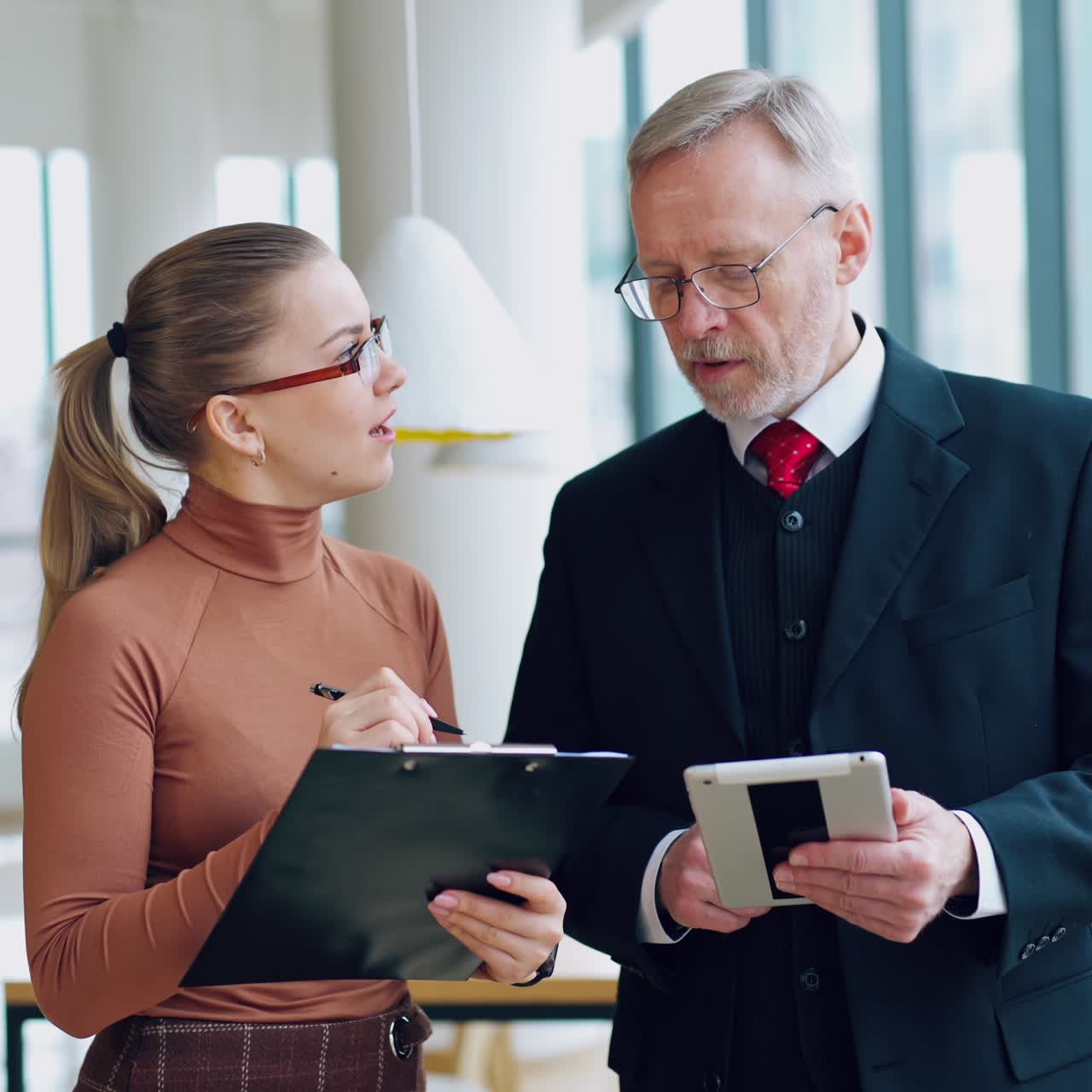 Director and woman discussing business project. Mature businessman talking to a young secretary with folder in the office.