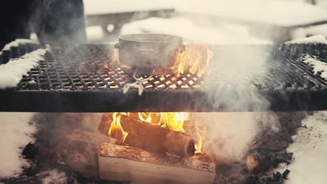 Boiling-hot-glogg-on-a-grill-over-campfire-in-woods-in-winter-in-Lemmenlaakso,-Finland