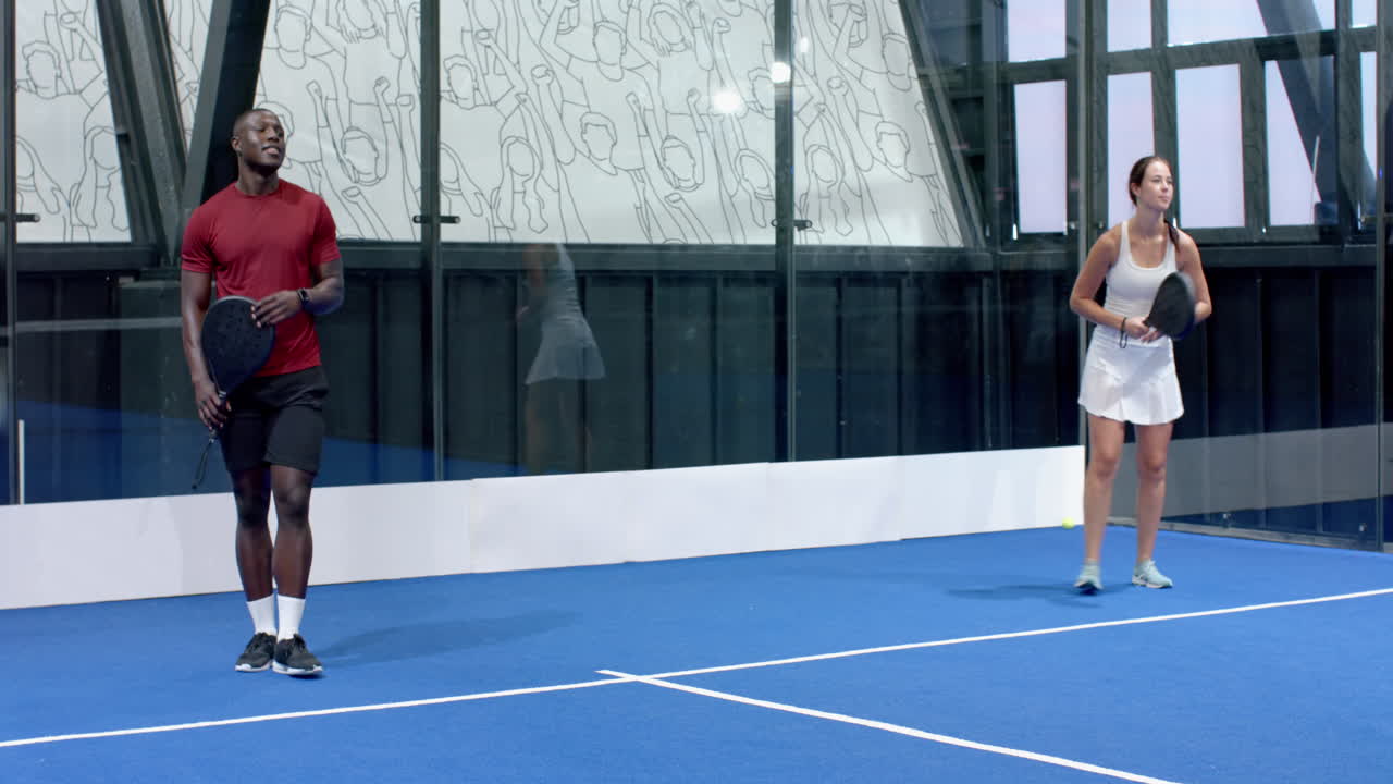 African American man and woman playing padel tennis on blue indoor court, focused and ready