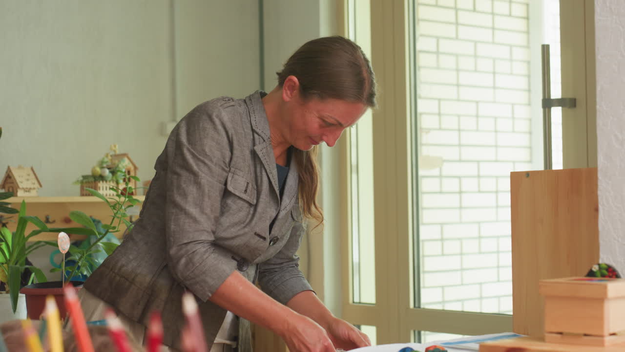 교사가 수업 시간에 달팽이를 상자에 다시 넣고, 호기심 많은 아이가 배경에서 지켜보는 동안 따뜻한 햇빛, 나무 선반, 식물, 몬테소리 교구 등이 있는 교실에서 조심스럽게 용기 뚜껑을 밀어 넣고 있어요.